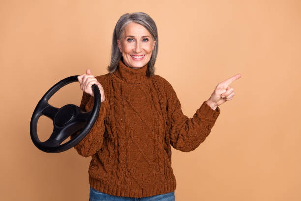 istock Elderly woman holding a steering wheel and smiling while pointing to the side 2197944623