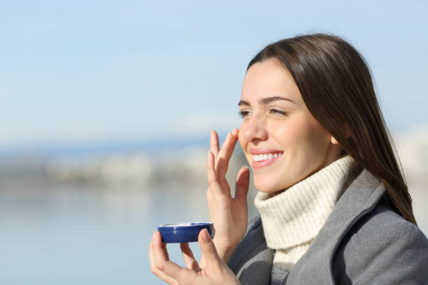 istock Happy woman in winter applying hydration cream on cheek 2197946570