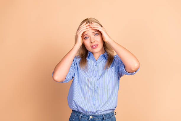 istock Young woman touching her forehead while appearing confused, standing against a beige background 2197949535