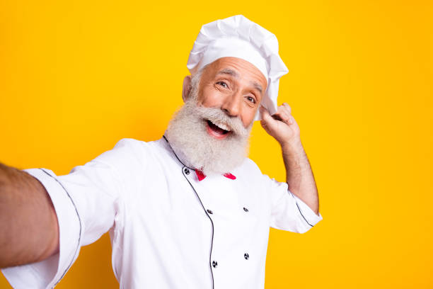 istock Happy senior chef in uniform posing with enthusiasm on bright yellow background, promoting culinary joy and gourmet cooking. 2197953897