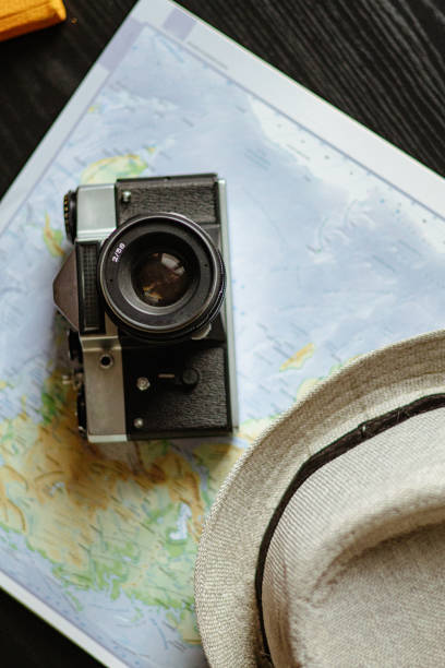Travel planning. Vintage film camera, world map and straw hat on rustic black table.