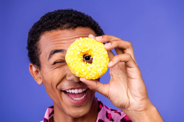 istock Cheerful Young Man Holding a Donut Against a Purple Background 2197954183