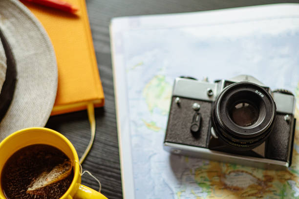 Travel planning. Vintage film camera, world map and straw hat on rustic black table.