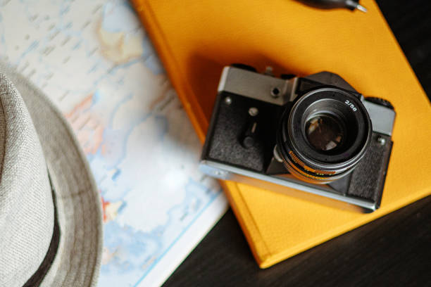 Travel planning. Vintage film camera, world map and straw hat on rustic black table.