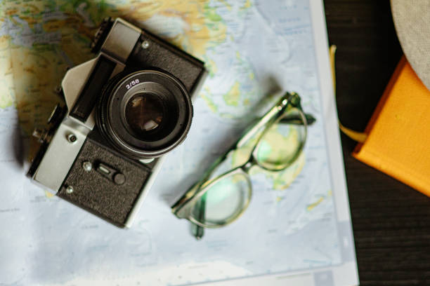 Travel planning. Vintage film camera, world map and straw hat on rustic black table.
