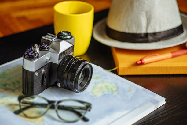 Travel planning. Vintage film camera, world map and straw hat on rustic black table.