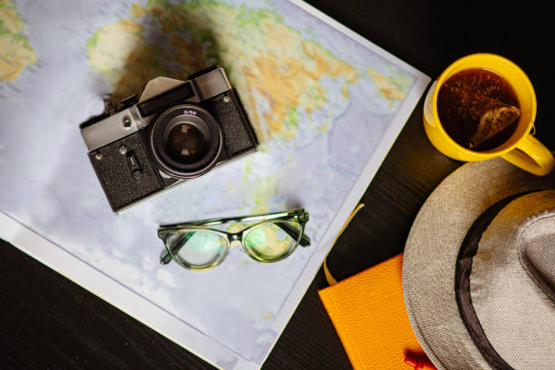 Travel planning. Vintage film camera, world map and straw hat on rustic black table.