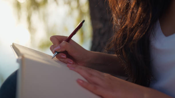 istock Beautiful young woman relaxing by lake and writing diary 2197962541