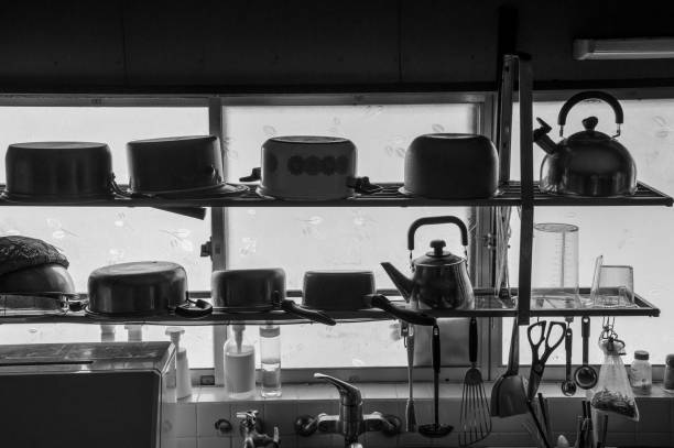 In the dark kitchen of a single person, the kitchen utensils that are regularly used are lined up on a shelf by the window.