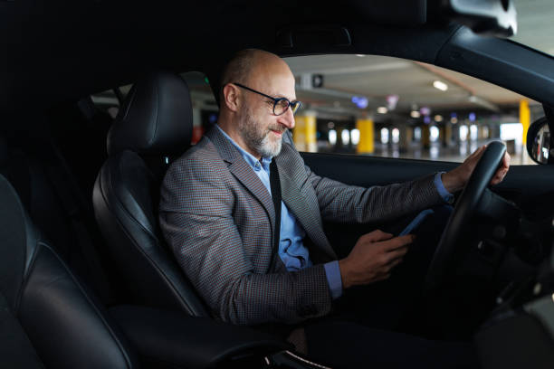 istock A smiling man sends messages on his mobile phone while sitting in the driver's seat 2197965613
