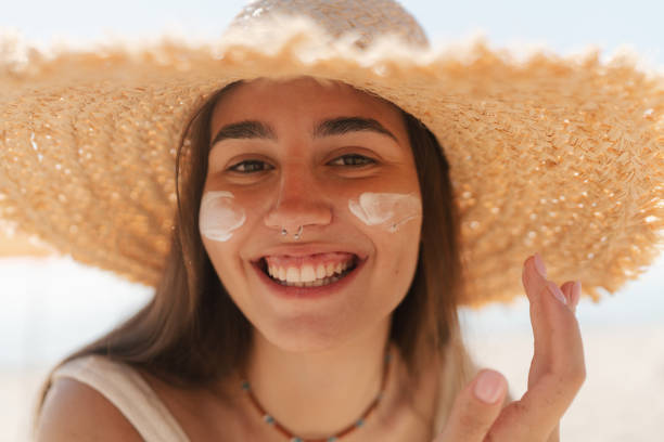istock Young woman applying sunscreen on her face while at the beach 2197971599