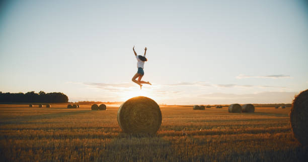 istock Carefree Young Woman Jumping on Haystack at Sunset 2197976617