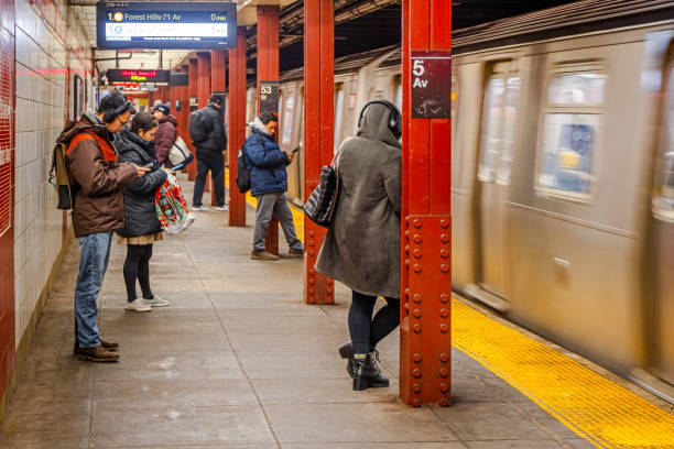 New York Subway, 5th Avenue Station, Manhattan, New York, United States - January 6th 2025:  People in winter clothes checking their smart phones while waiting for the arriving subway train