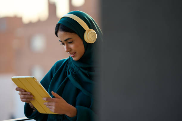 istock Muslim woman wearing headphones using digital tablet while smiling 2197977723