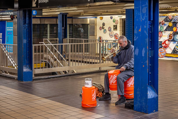 New York Subway, Times Square Station, Manhattan, New York, United States - January 17th 2025:  Man playing a trumpet while making the rhythm on a plastic bin in the famous underground subway station