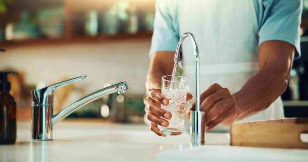 persona, rubinetto e mani con bicchiere d'acqua in cucina per bevanda fresca, liquido e idratazione. lavello primo piano, assetato o versando bevanda pura in contenitore per la nutrizione, bere o filtrazione a casa - bere foto e immagini stock