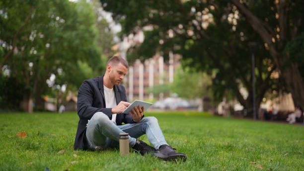 istock Young Professional Businessman Sitting on Grass, Using a Digital Tablet in a City Park 2197990289