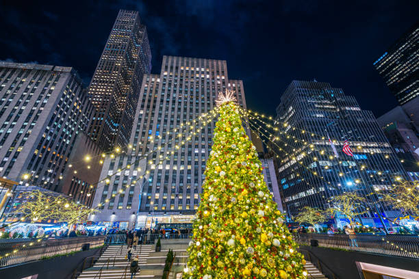 Festive display of a luminous Christmas tree with surrounding skyscrapers visited by people in the holiday season in New York City.