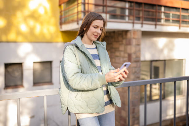 istock Young woman smiling while using her smartphone outdoors in a modern urban setting during the day 2197994646