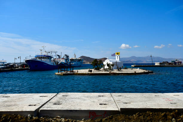 Naxos, Greece - September 20, 2024: a small island in the harbor of Naxos with a chapel on it and trawler and ferry