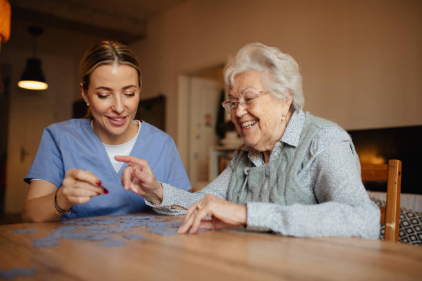 Friendly caregiver and elderly patient working on puzzle together, having fun. stock photo