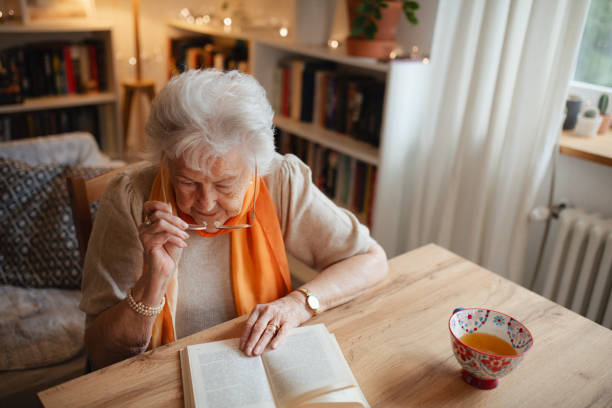 istock Lovely elderly lady reading a book, sitting at the kitchen table and sipping tea. 2197998948