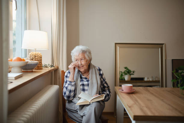 istock Lovely elderly lady reading a book, sitting at the kitchen table and sipping tea. 2197999693