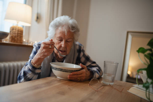 istock Poor elderly woman eating soup at the dining table. 2197999723