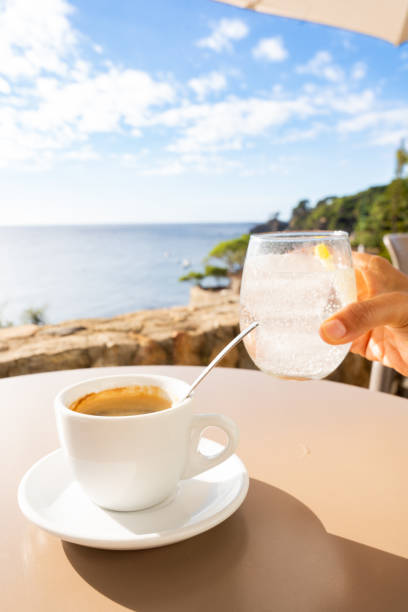 istock Ceramic coffee mug beside sparkling water glass on wooden table, ocean horizon visible, peaceful morning atmosphere with relaxing coastal view 2198005462