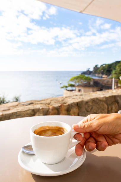 istock Hand gripping steaming coffee mug near ocean horizon, soft blue sky creating serene coastal moment 2198005545