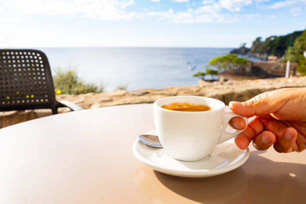 istock Hand gripping steaming coffee mug near oceanfront window, serene blue waters stretching beyond wooden surface, embodying tranquil morning stillness 2198005559