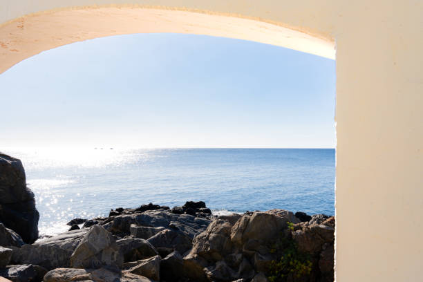 istock Rugged rocky arch bordering vivid blue seascape, sunlight streaming across tranquil summer ocean horizon with clear skies in the Mediterranean Sea. 2198005592