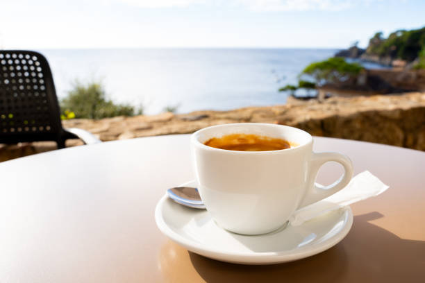 istock Steaming coffee resting on a table, overlooking a serene ocean view with clear blue skies and distant greenery 2198005636