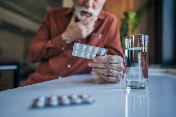 istock An elderly man sits at the kitchen table, his figure blurred in the background, while the focus remains on his weathered hands holding a few pills. 2198006773
