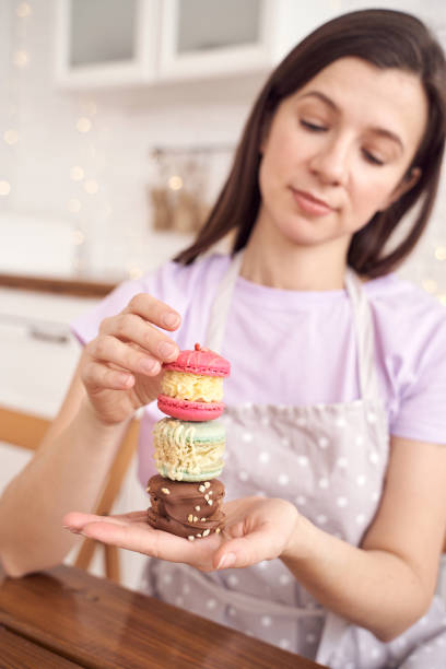 istock Smiling woman balancing colorful macarons on hand in bright kitchen, showcasing 2198007426