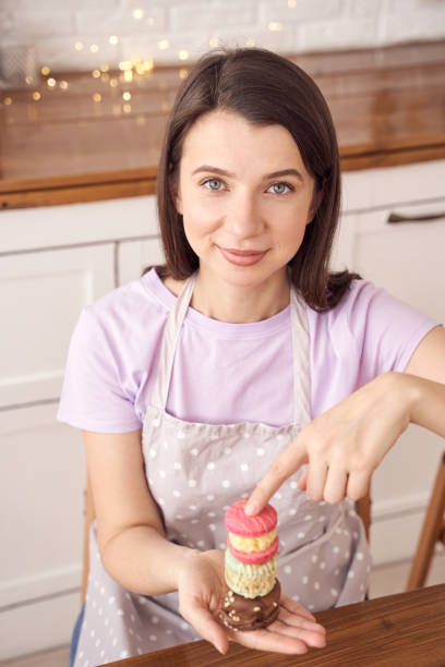istock Woman in polka dot apron showing colorful macarons in cozy kitchen setting 2198007432