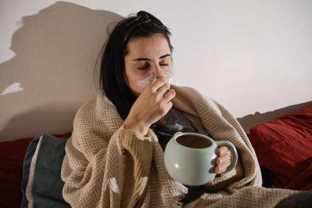 istock Woman in a Blanket Blowing Her Nose While Sipping Tea 2198025368