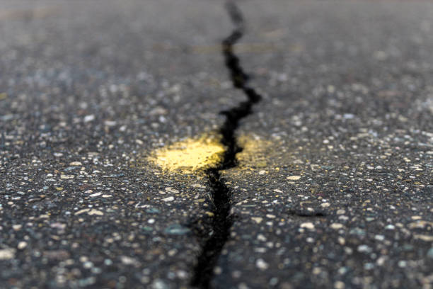 low angle view of long crack in road marked for repair. abstract concept for obstacles, uncertainty, meeting challenges, danger ahead, widening gap disruption navigation construction season background