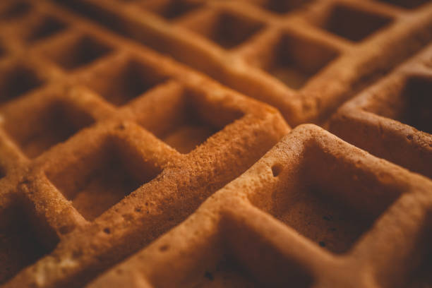 Golden-brown crispy waffles in a close-up shot. Detailed texture with a crisp outer layer and soft interior. Freshly baked breakfast food with a warm and inviting appearance.