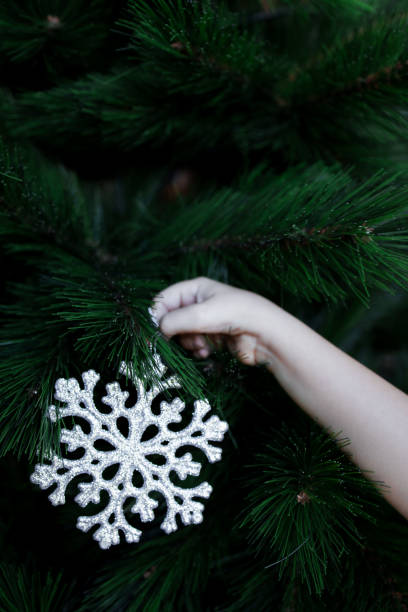 Childs hand decorating Christmas tree with silver snowflake ornament.