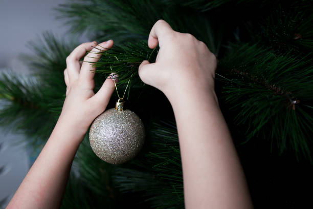 Childs hands decorating Christmas tree with glittering bauble ornament