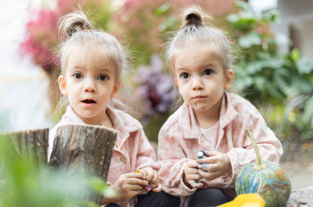 Color image of happy, twin, blonde-haired girls sitting together outside on a summer day.