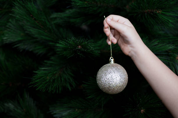 istock Childs hand hanging gold bauble on Christmas tree branch 2198030490