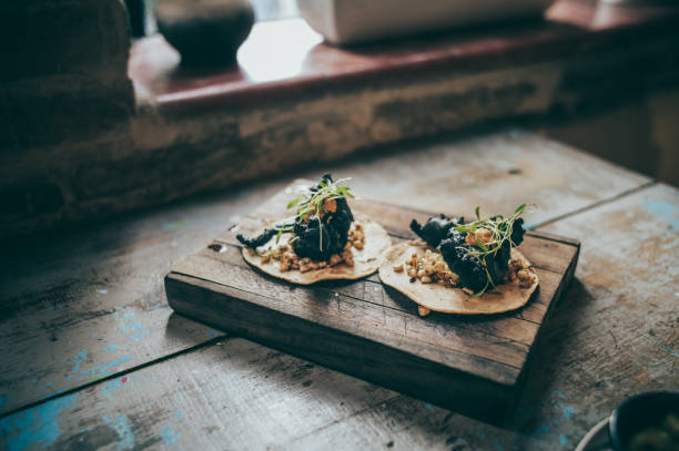 Charcoal crab tacos with corn kernels, served on a wooden board.