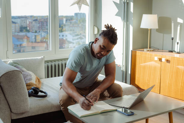 istock African America man working remotely at home while writing notes and using a laptop 2198040643