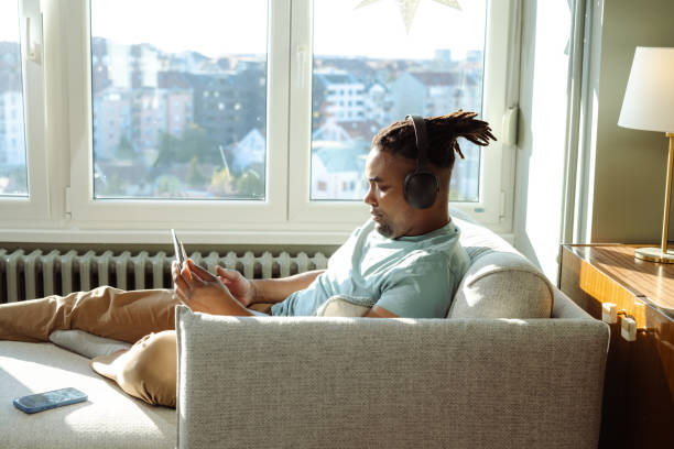 istock Young man relaxing on a couch using headphones and browsing on a laptop 2198040748