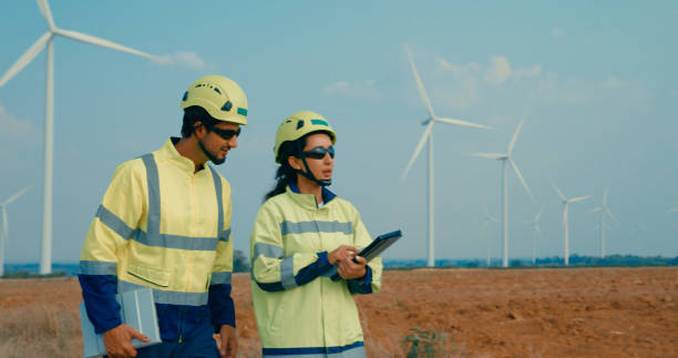 istock Renewable energy engineers walking consult digital tablet while working on maintenance and efficiency of wind turbines in rural. Green ecological power generation wind sustainable energy. 2198048400