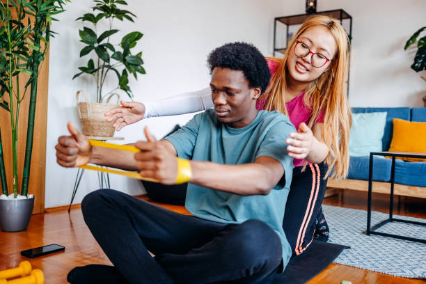 istock Friends having fun exercising together at home stretching rubber band 2198052668