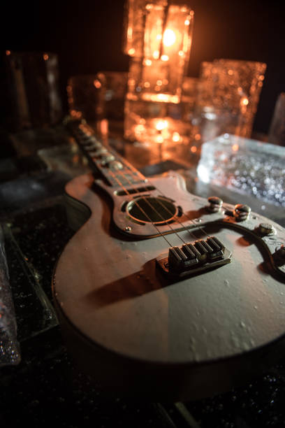 Music Concept: Guitar Miniature on a Dark Background with Vivid Light, Smoke, and Fire Effects. Golden electro guitar under a Dramatic Spotlight. Ice Glass blocks decor