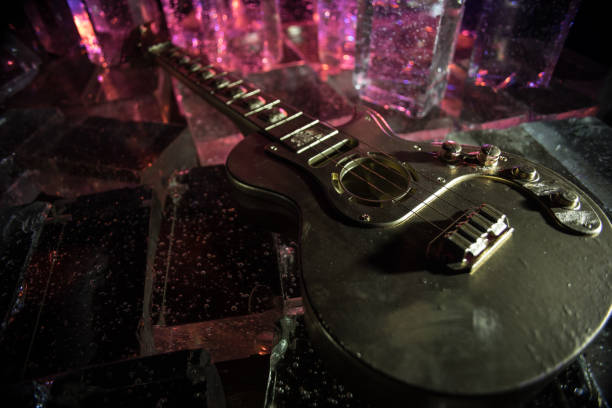 Music Concept: Guitar Miniature on a Dark Background with Vivid Light, Smoke, and Fire Effects. Golden electro guitar under a Dramatic Spotlight. Ice Glass blocks decor
